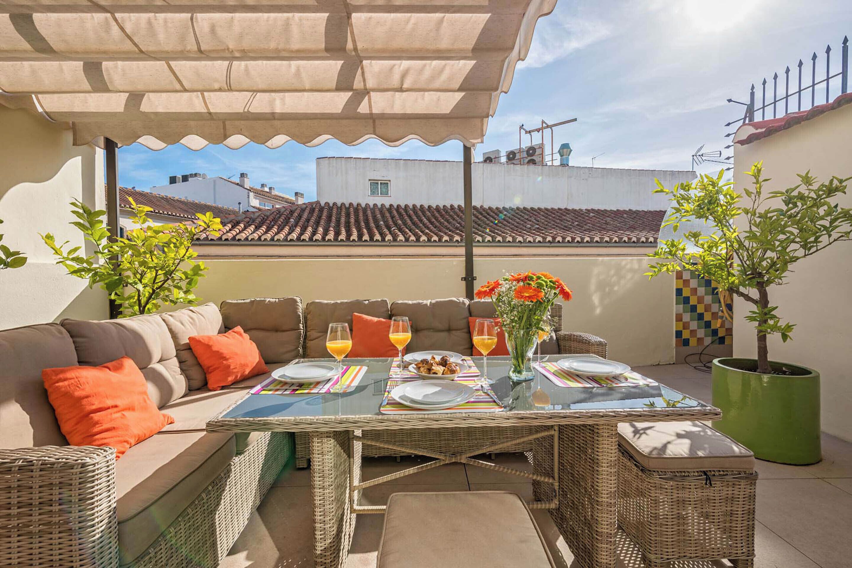An outdoor patio with a glass-top table, wicker furniture, and a view of buildings in the background.
