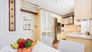 A modern kitchen with white cabinets, a stainless steel refrigerator, and a dining area with a white table and chairs. - Solaga - Emma (Málaga)