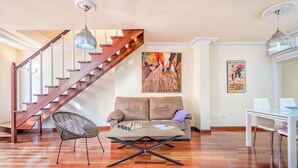 A spacious living room with a wooden staircase, a sofa, a coffee table with chess pieces, and a dining area. - Solaga - Emma (Málaga)