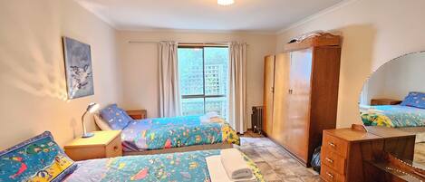 Ein Schlafzimmer mit zwei Betten, einem Kleiderschrank, einem Schreibtisch und einem Fenster mit Vorhängen.