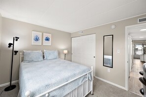 A bedroom with a bed, a standing lamp, a door, and a mirror.