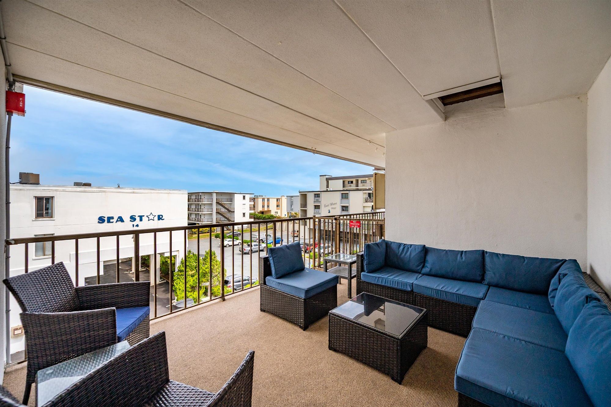 A balcony with wicker furniture, a glass table, and a view of a building with 'SEA STAR' signage.