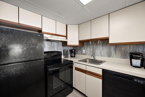 A modern kitchen with a black refrigerator, a stove, a dishwasher, and a coffee maker.