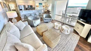 A modern living room with a sofa, armchairs, ottomans, a television, and a balcony with a view. - Best views and close to the beach! 7801 L1 (Miramar Beach)