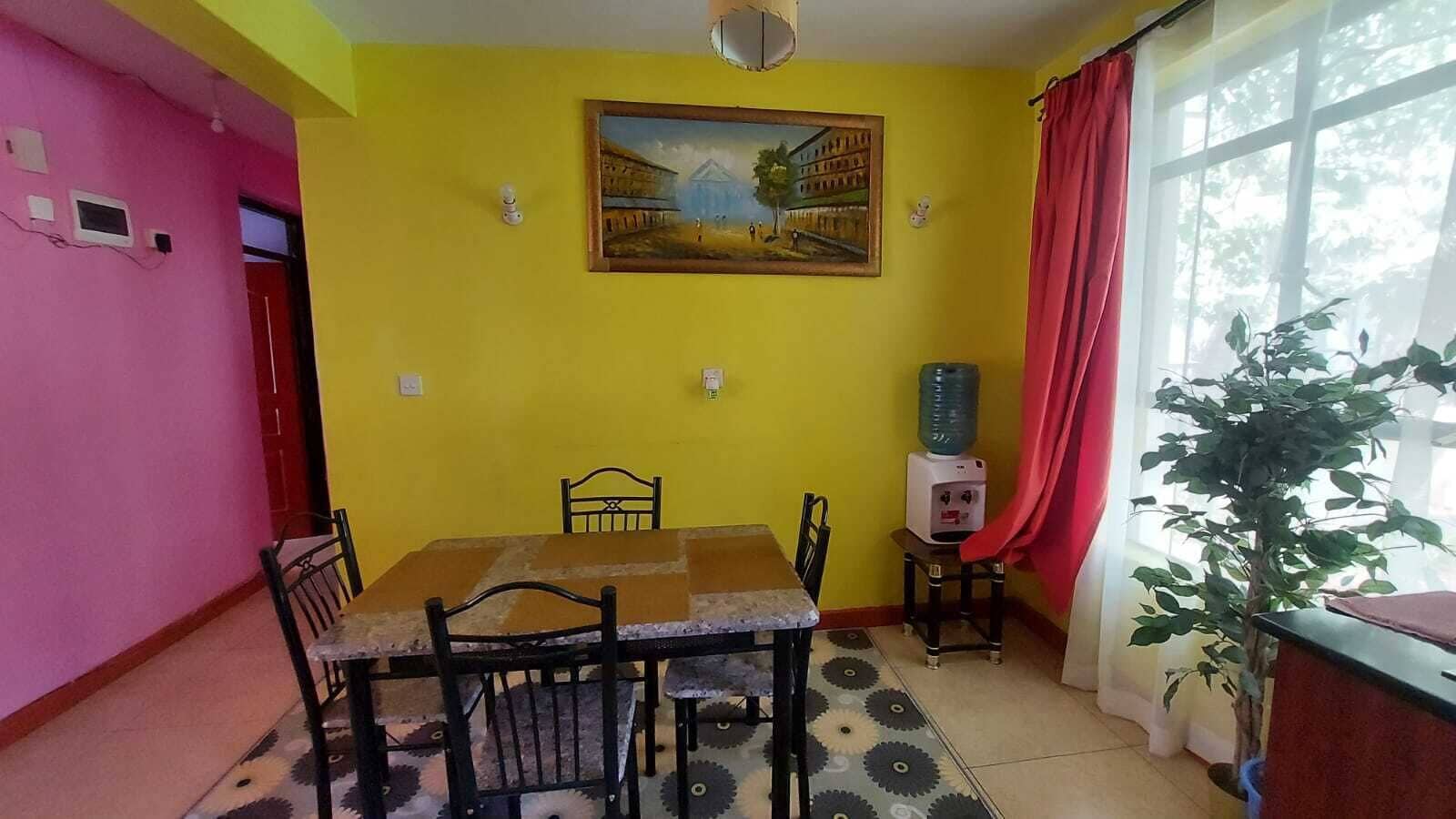 A dining area with a table and chairs, a water dispenser, a painting on the wall, and a window with a plant.