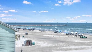 En strand med parkerade bilar, tält och en pir i bakgrunden.