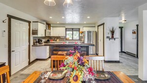 A modern kitchen with a central island, wooden dining table, and a floral centerpiece. - Deck & Mtn Views: Libby Home on Golf Course! (Libby)