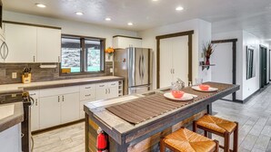 A modern kitchen with a central island, stainless steel appliances, and a large window. - Deck & Mtn Views: Libby Home on Golf Course! (Libby)