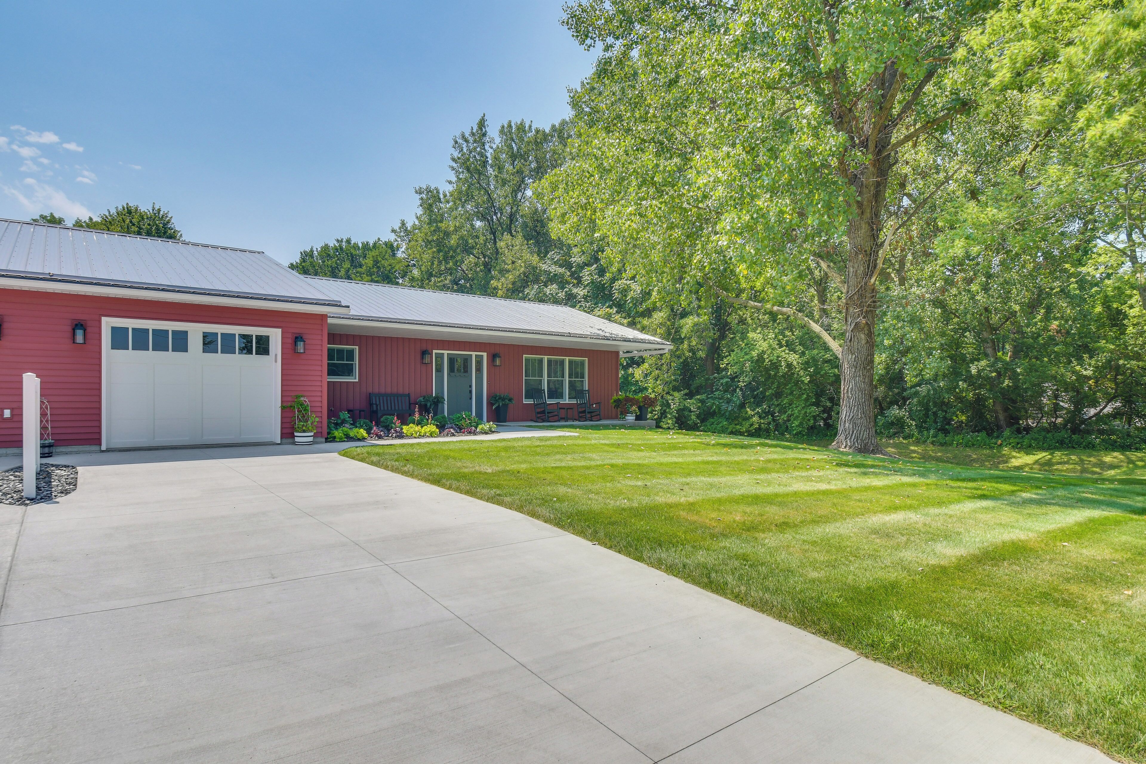 A red single-story house with a garage, a front lawn, and a large tree.