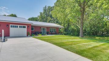 A red single-story house with a garage, a front lawn, and a large tree.