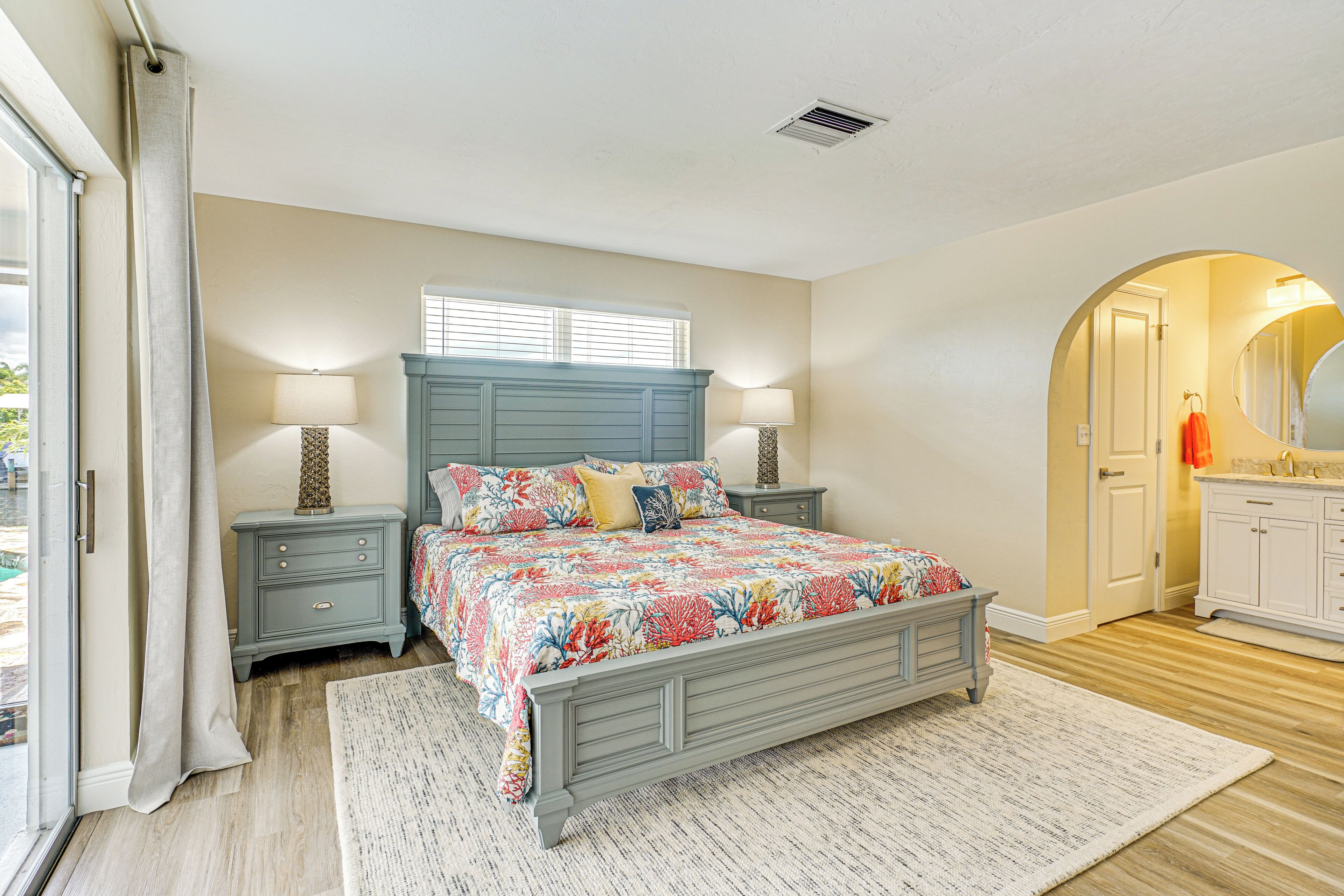 A bedroom with a bed, nightstands, a window, and a bathroom with a mirror and sink.