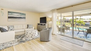 Una sala de estar con sofá, sillón, televisor de pantalla plana y vista a una piscina a través de amplios puertas corredizas de vidrio.
