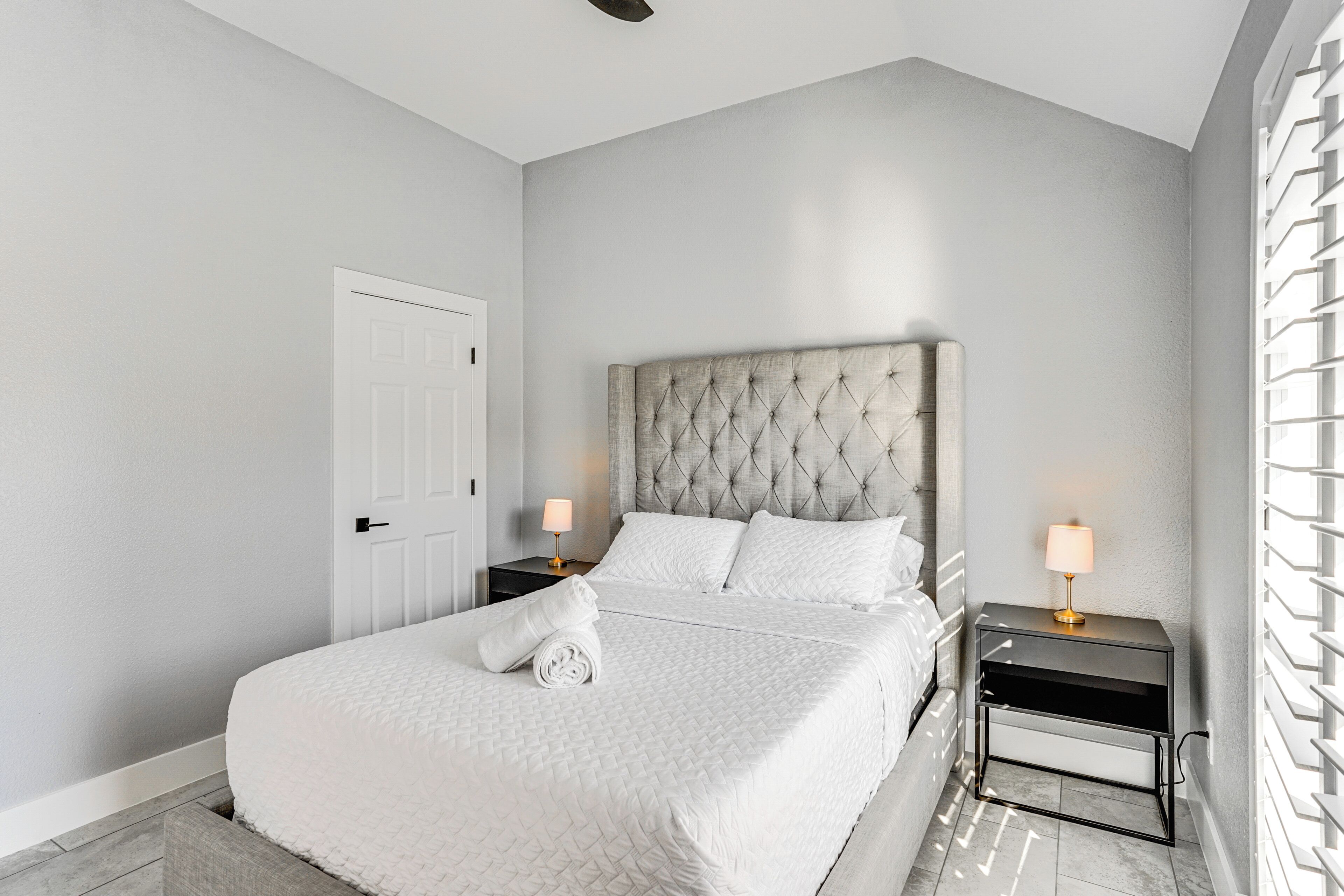 A neatly made bed with white bedding, a tufted headboard, and a bedside table with a lamp.