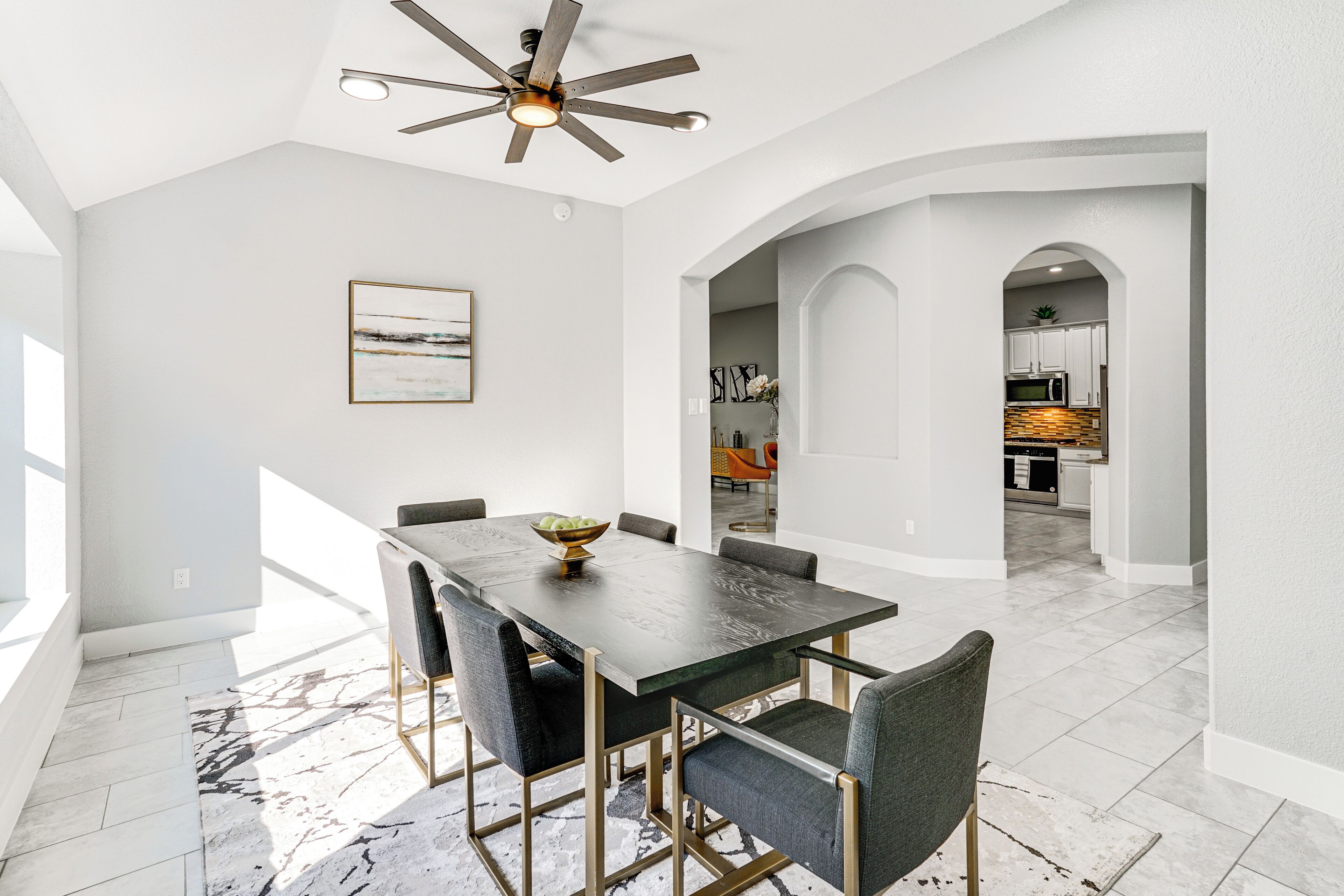 A dining area with a dark wooden table, six chairs, and a ceiling fan.