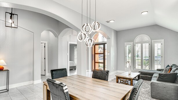 Amplia sala de estar con una mesa de comedor de madera, sofás grises y un ventanal con contraventanas.