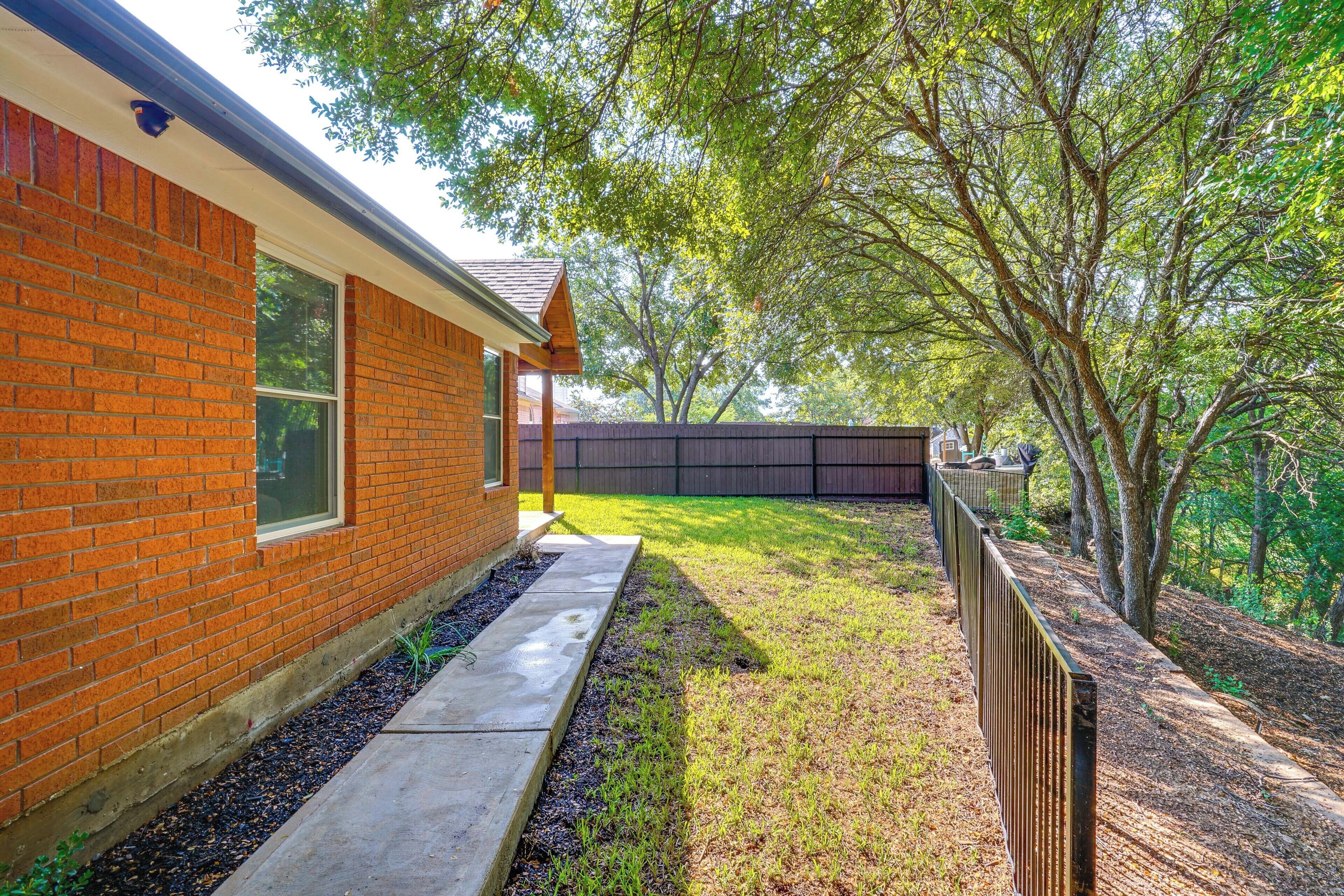 A brick house with a visible window and a concrete pathway leading to a fenced yard.