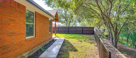 A brick house with a visible window and a concrete pathway leading to a fenced yard.