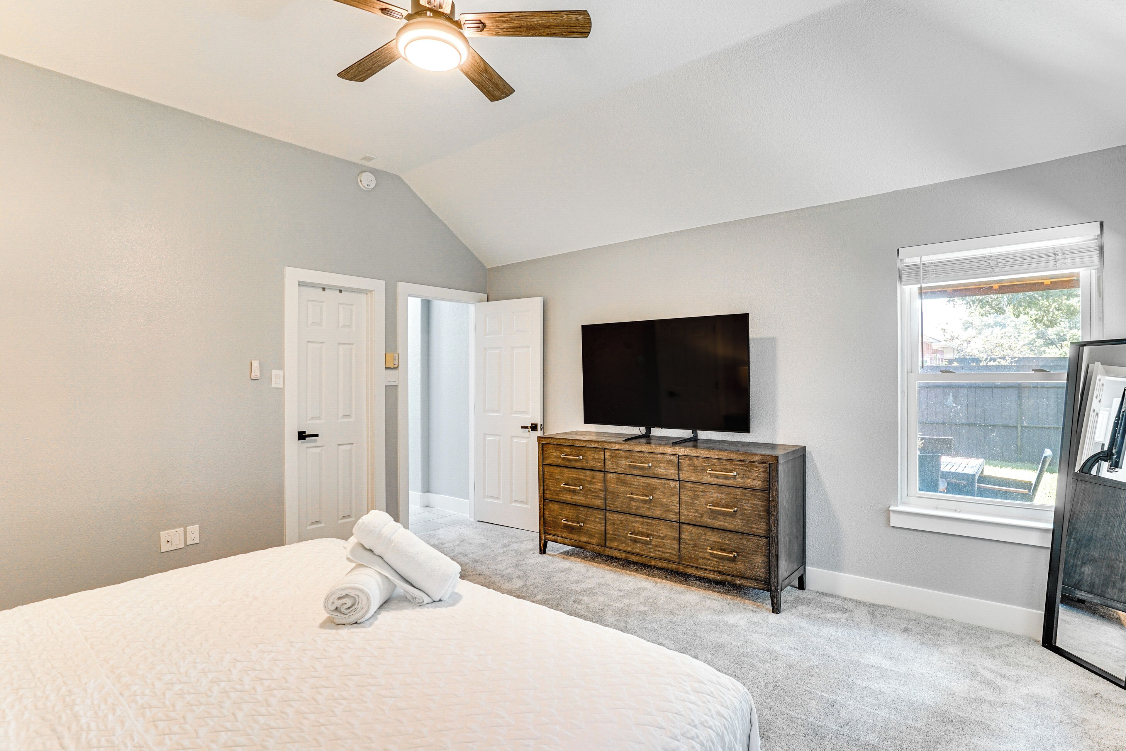 A bedroom with a large bed, a wooden dresser, a TV, and a window with blinds.
