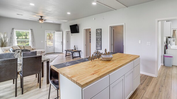 Una cocina moderna con una isla de madera, armarios blancos y un comedor con mesa y sillas.