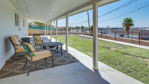 Eine überdachte Terrasse mit Sitzgelegenheit, Blick auf die Straße und eine Rasenfläche.