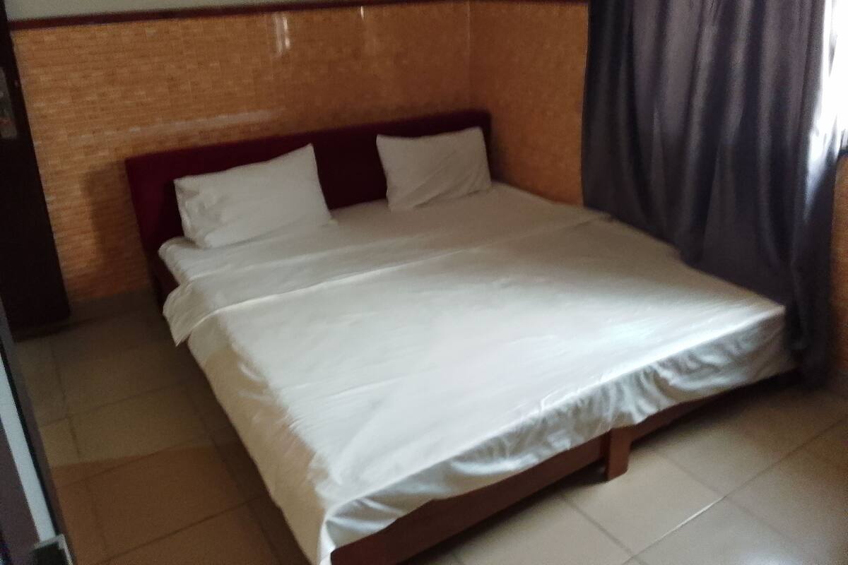A standard hotel room with a bed, a wooden headboard, and a curtain.