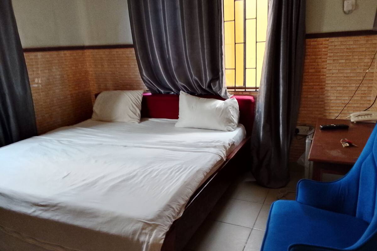 A single bed with white bedding, a red headboard, and a blue chair.