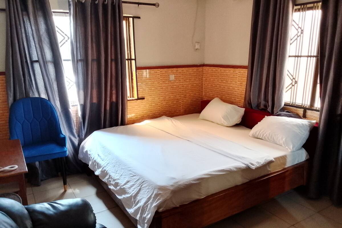 A hotel room with a large bed, a blue chair, and a wooden headboard.