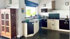 A modern kitchen with a large window, built-in cabinets, and a wooden cabinet with drawers. - Villa Vaïtea, pool, sea view, 3 bedrooms, Leroux area (Deshaies)