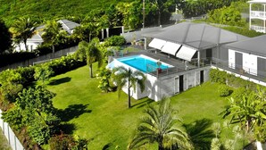 A residential property with a swimming pool, lush greenery, and a view of distant hills. - Villa Vaïtea, pool, sea view, 3 bedrooms, Leroux area (Deshaies)