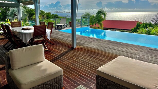 A covered outdoor area with a pool, wooden deck, wicker furniture, and a view of the sea. - Villa Vaïtea, pool, sea view, 3 bedrooms, Leroux area (Deshaies)