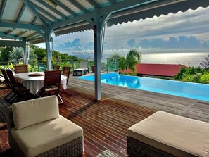Ein überdachter Außenbereich mit Pool, Holzterrasse, Korbmöbeln und Meerblick.