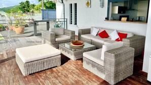 A covered outdoor seating area with wicker furniture, a glass balustrade, and potted plants. - Villa Vaïtea, pool, sea view, 3 bedrooms, Leroux area (Deshaies)