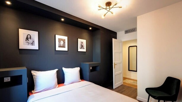 Ein modernes Hotelzimmer mit einem großen Bett, einem schwarzen Sessel und gerahmten Bildern an der Wand.
