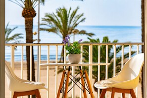 A balcony with a view of the ocean, two white chairs, a potted plant with purple flowers, and a pair of pruning shears.