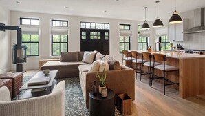 Ein modernes Wohnzimmer mit einer Couch, einem Couchtisch und einem Kamin. Es gibt eine Küchenzeile mit einer Bar und Hockern.