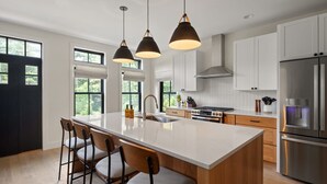 A modern kitchen with a large island, white cabinetry, stainless steel appliances, and pendant lighting.