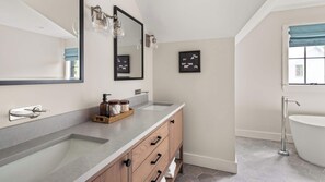 Een moderne badkamer met een grote spiegel, twee wasbakken, een houten wastafelmeubel en een vrijstaand bad.