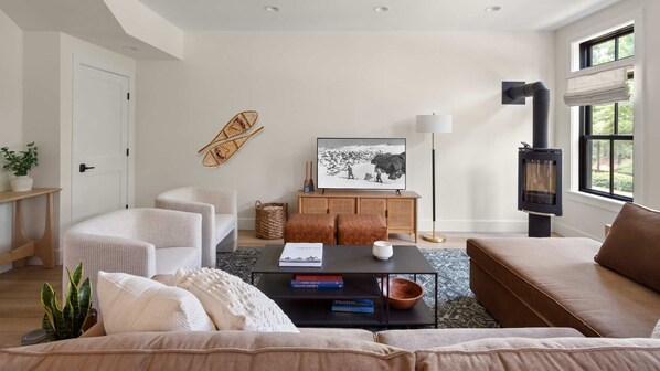 Een moderne woonkamer met een bank, fauteuils, een salontafel, een open haard, een televisie en een boekenkast.