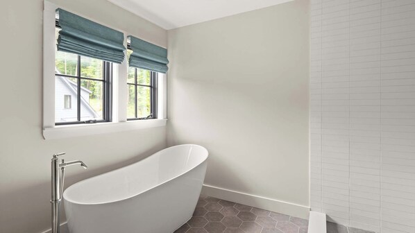 A bathroom with a freestanding bathtub, a window with a view of a house, and a tiled wall. - 5BR Luxury Townhome | Stowe | More Units Available (Thunderbolt)