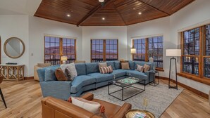 A spacious living room with a large sectional sofa, a coffee table, and a view of mountains through large windows. - Extraordinary Location For Large Groups | Apex Grande (Steamboat Springs)
