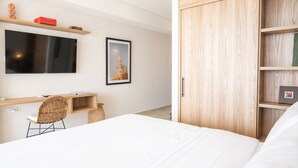 Un dormitorio moderno con cama, escritorio, silla, televisor y armario.