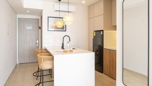 Una cocina moderna con una isla central, dos sillas de mimbre, un refrigerador y una lámpara colgante.