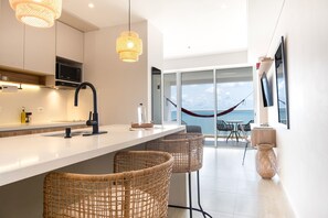 A modern kitchen with a white countertop, black faucet, and wicker chairs. There is a large window with a view of the sea and a hammock. - w Dazzling Loft w Ocean View in Crespo (Cartagena)