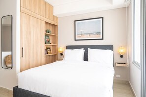 A neatly arranged bedroom with a bed, wooden shelving, a framed picture of a beach, and bedside lamps. - w Dazzling Loft w Ocean View in Crespo (Cartagena)