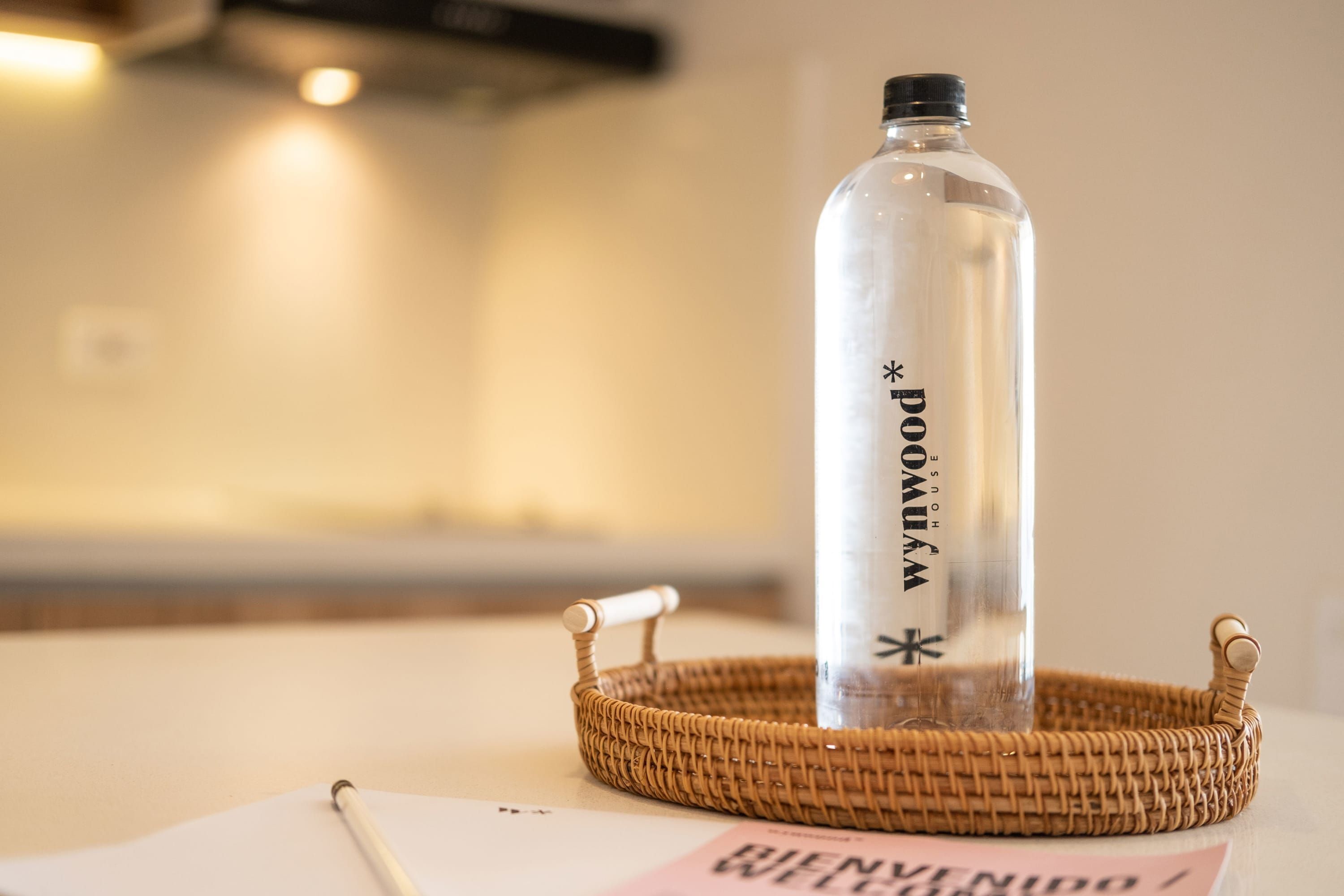A clear glass bottle with a black cap and a straw, placed on a woven basket.