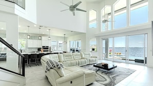 A spacious living area with a large white sofa, a coffee table, and a view of the ocean through large windows.