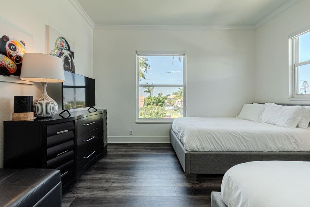 A bedroom with a bed, a dresser, a lamp, and a window with a view.