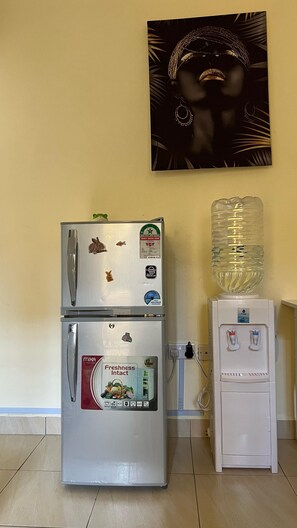 Compact kitchen area with a refrigerator, water dispenser, and framed picture.