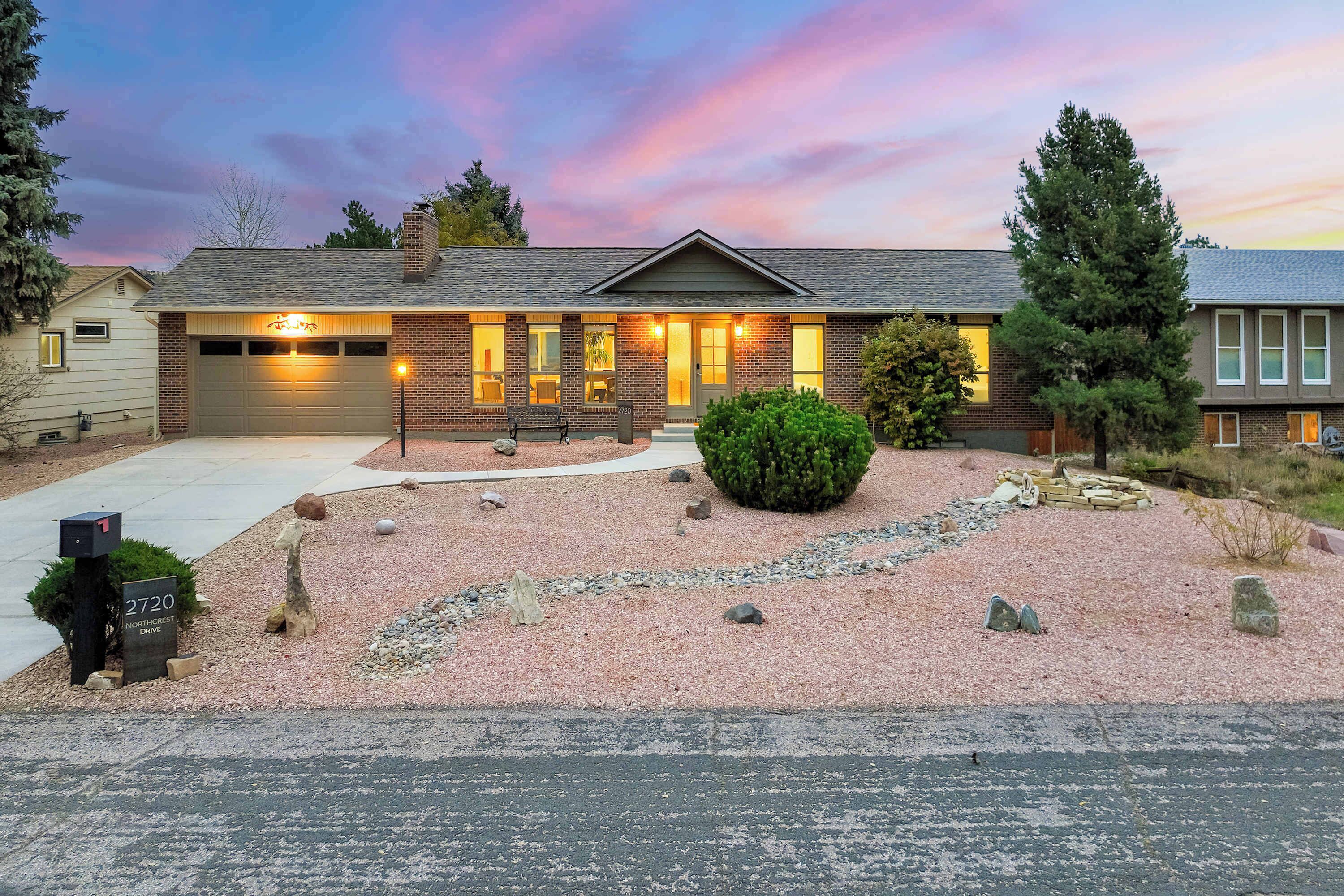 A two-story house with a garage, a front porch, and a well-maintained garden with gravel and rocks.