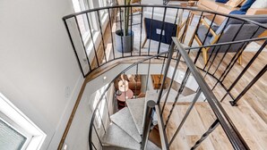 Un escalier en colimaçon avec une rampe en métal mène à un espace de vie comprenant un canapé et une table basse.